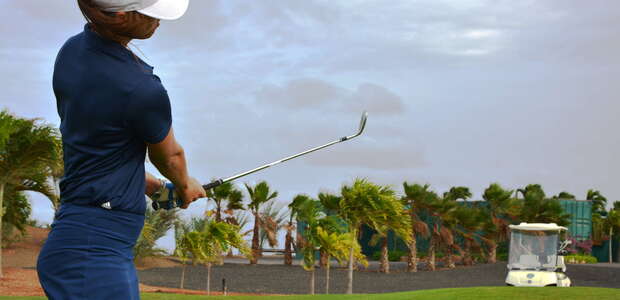 Golferin im blauen Outfit, im Hintergrund fährt ein Golfcaddy