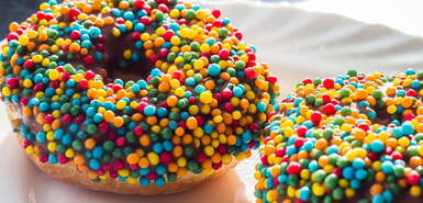 Zwei Donuts auf einem Teller mit Schokoüberzug und bunten runden Streuseln