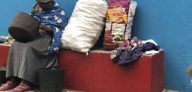 Frau sitzt auf einer Bank, neben ihr Säcke