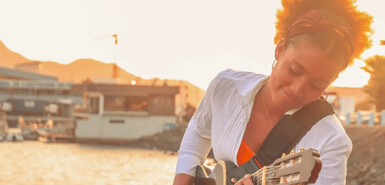 Kapverdische Musikerin Cláudia Sofia sitzt am Strand und spielt Gitarre